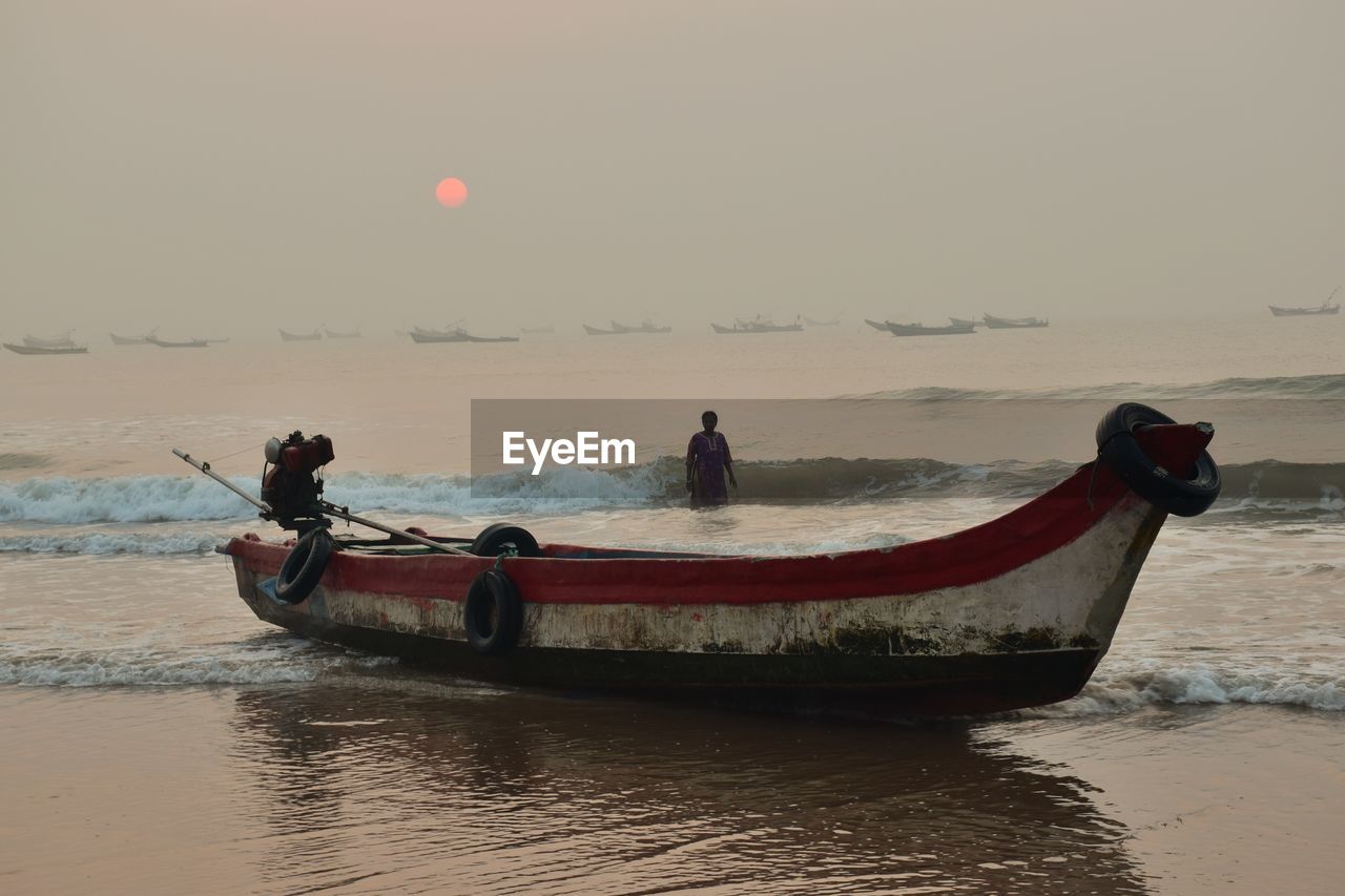 Fishing boat and woman in sea against sky during sunset