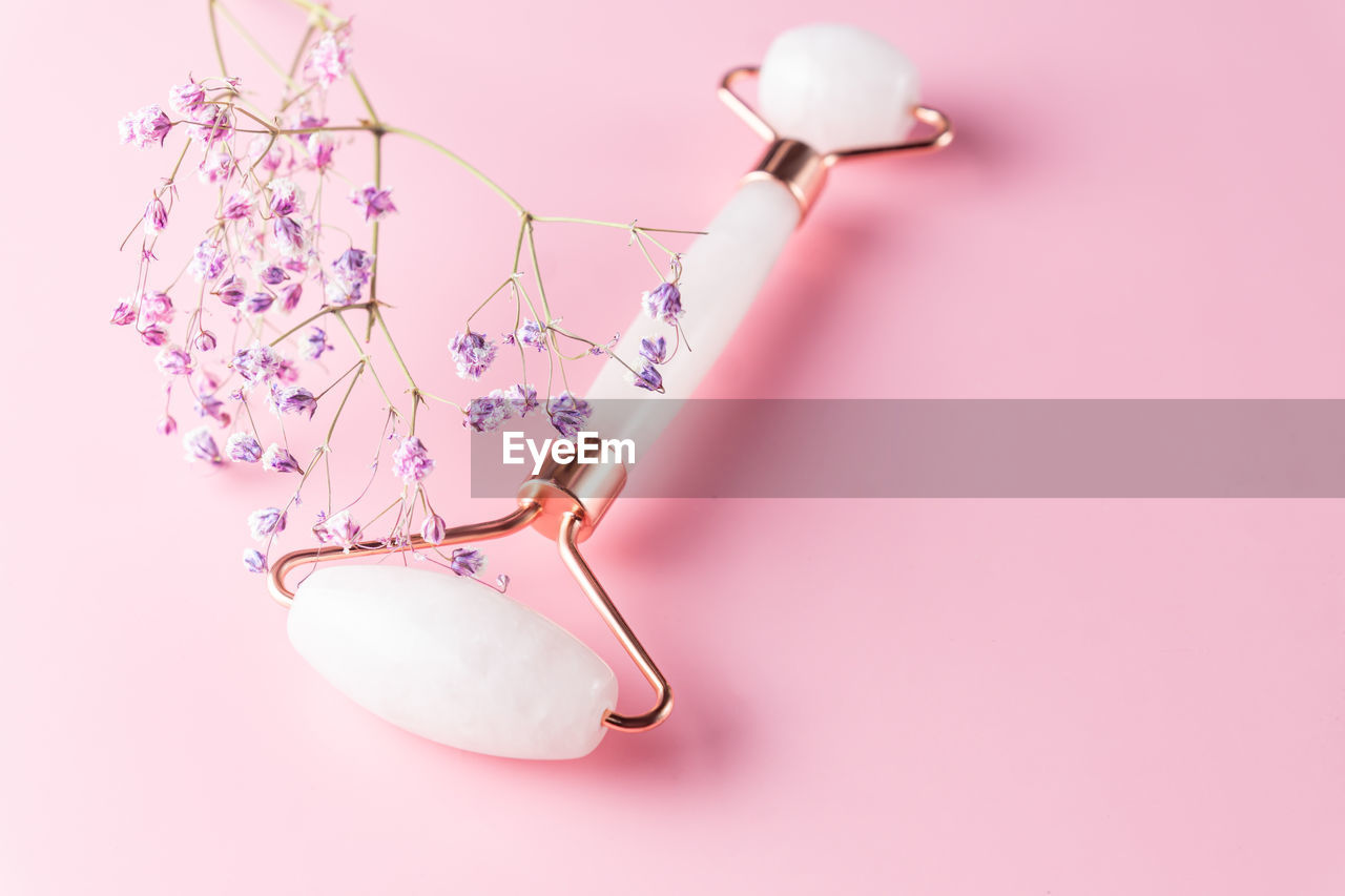 Face roller and gypsophila flower on pink background. massage tool for facial skin care, spa beauty