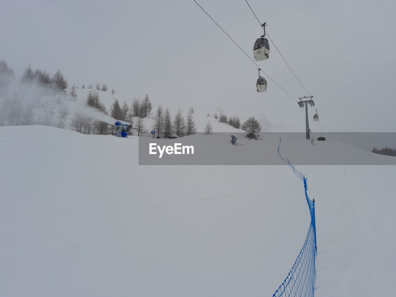 Close up of ski lift durino a snowfall with snow cannons belinda it ski on snow covered landscape