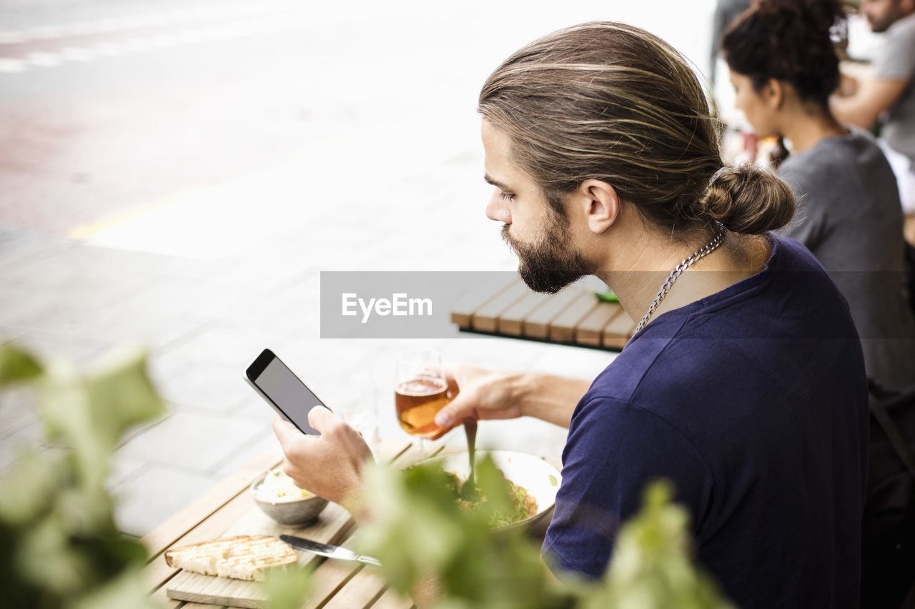 Man using mobile phone while having drink at sidewalk cafe