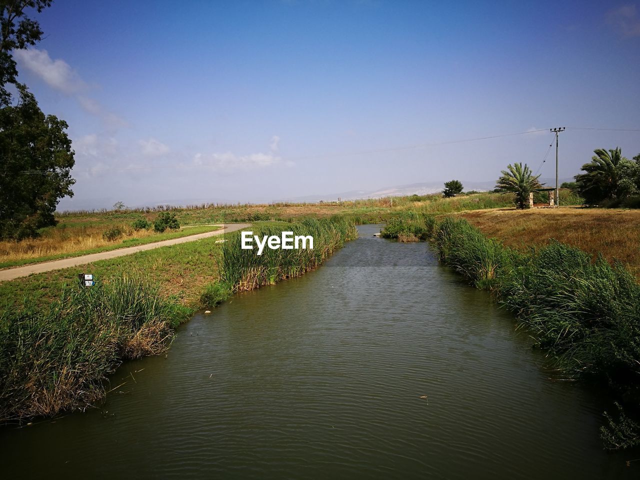 Scenic view of canal amidst field against sky