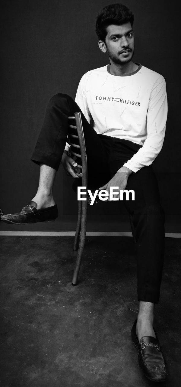 PORTRAIT OF A YOUNG MAN SITTING ON CHAIR