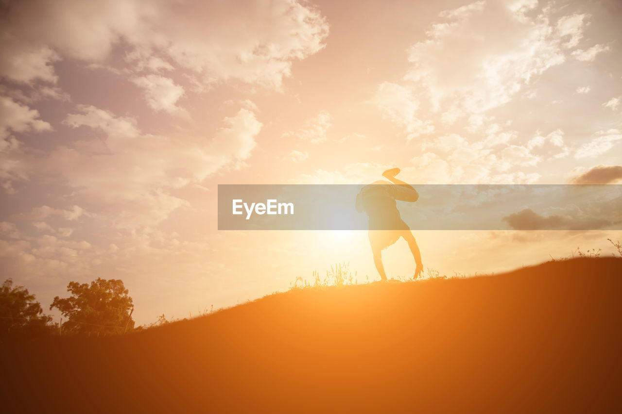 Silhouette man doing handstand on field against sky during sunset