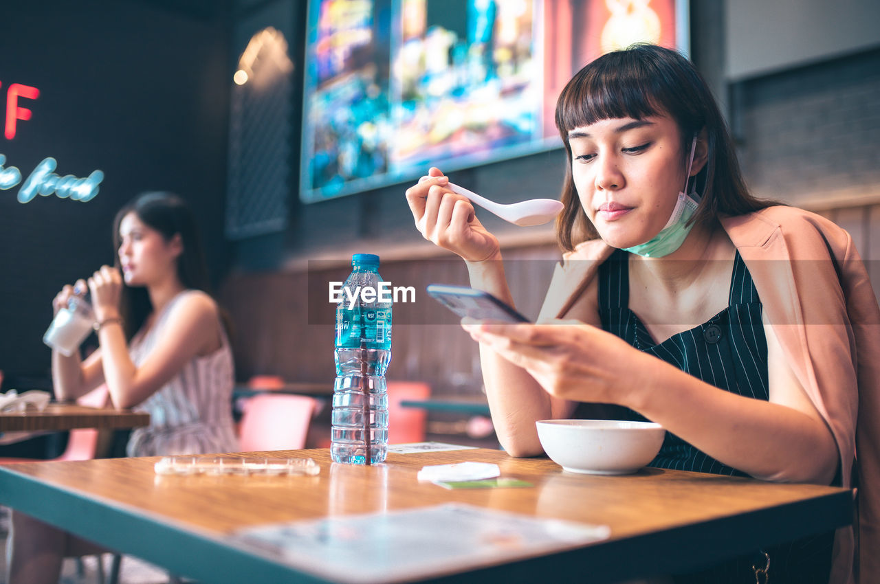 Young woman using phone while sitting on table at cafe