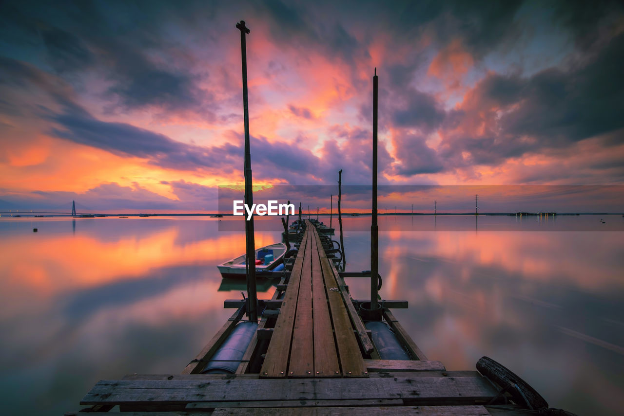 Low angle view of jetty in sea against sunset sky