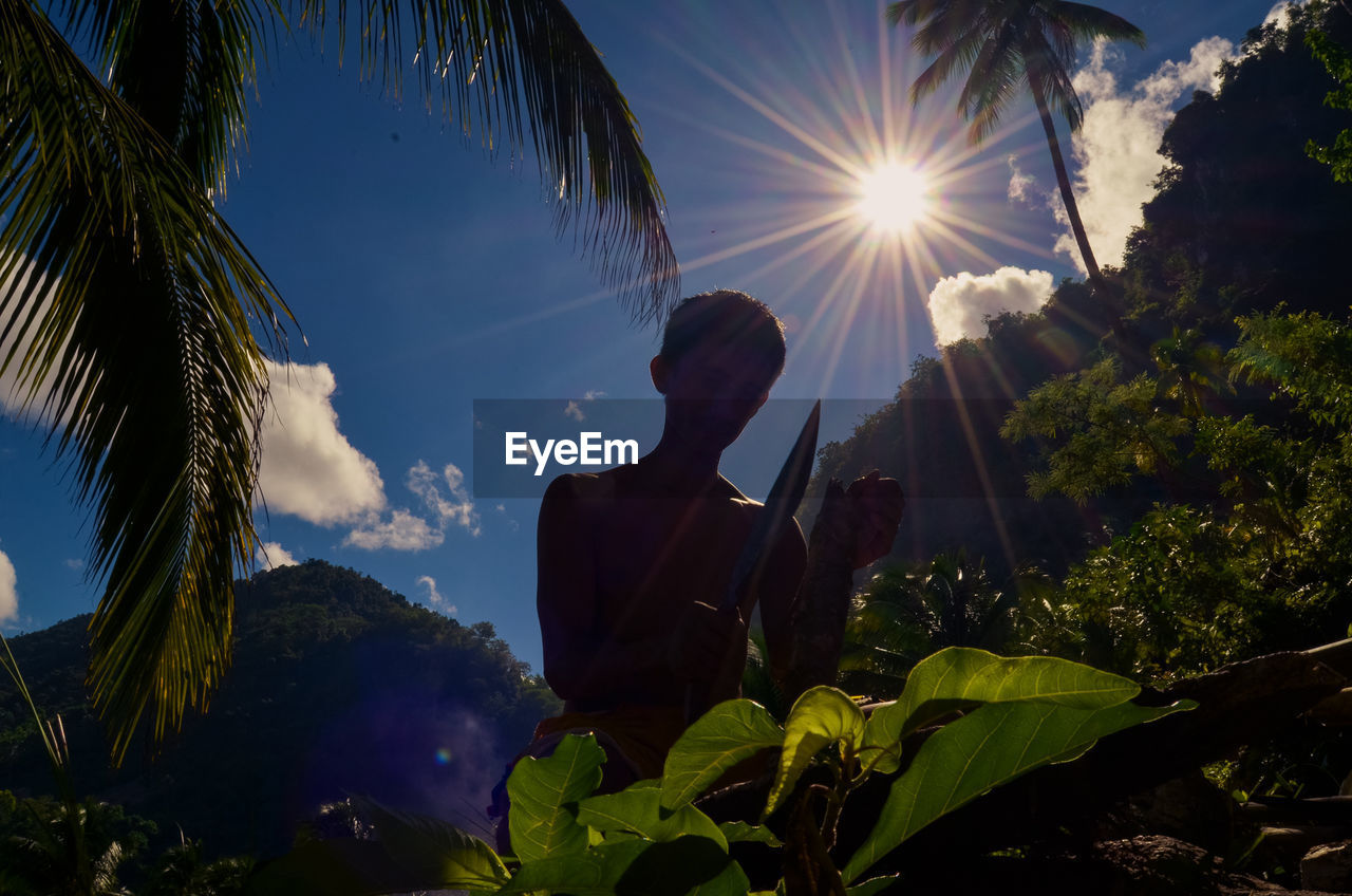 LOW ANGLE VIEW OF PERSON STANDING BY PLANTS AGAINST SKY