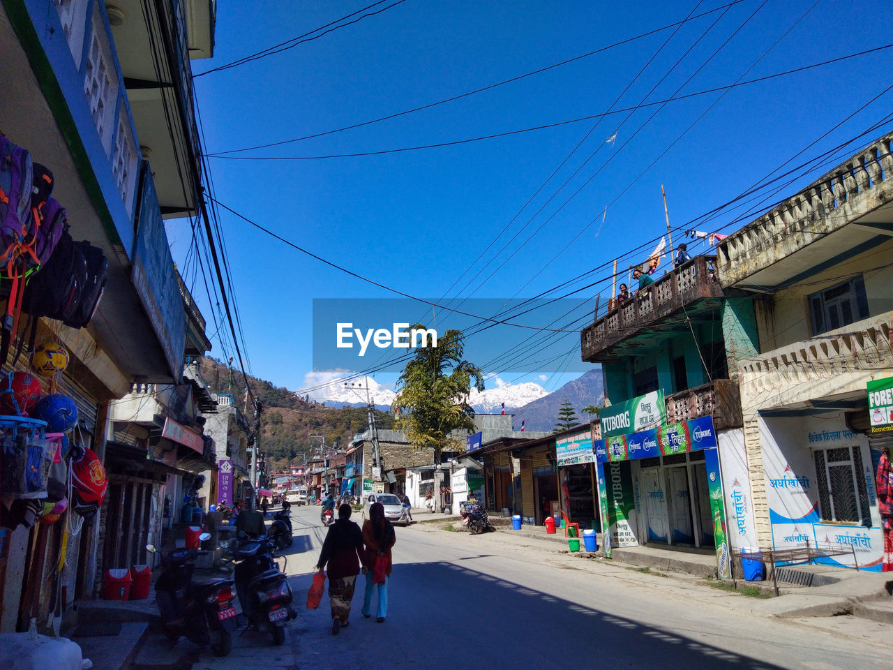 PEOPLE WALKING ON STREET AMIDST BUILDINGS AGAINST BLUE SKY