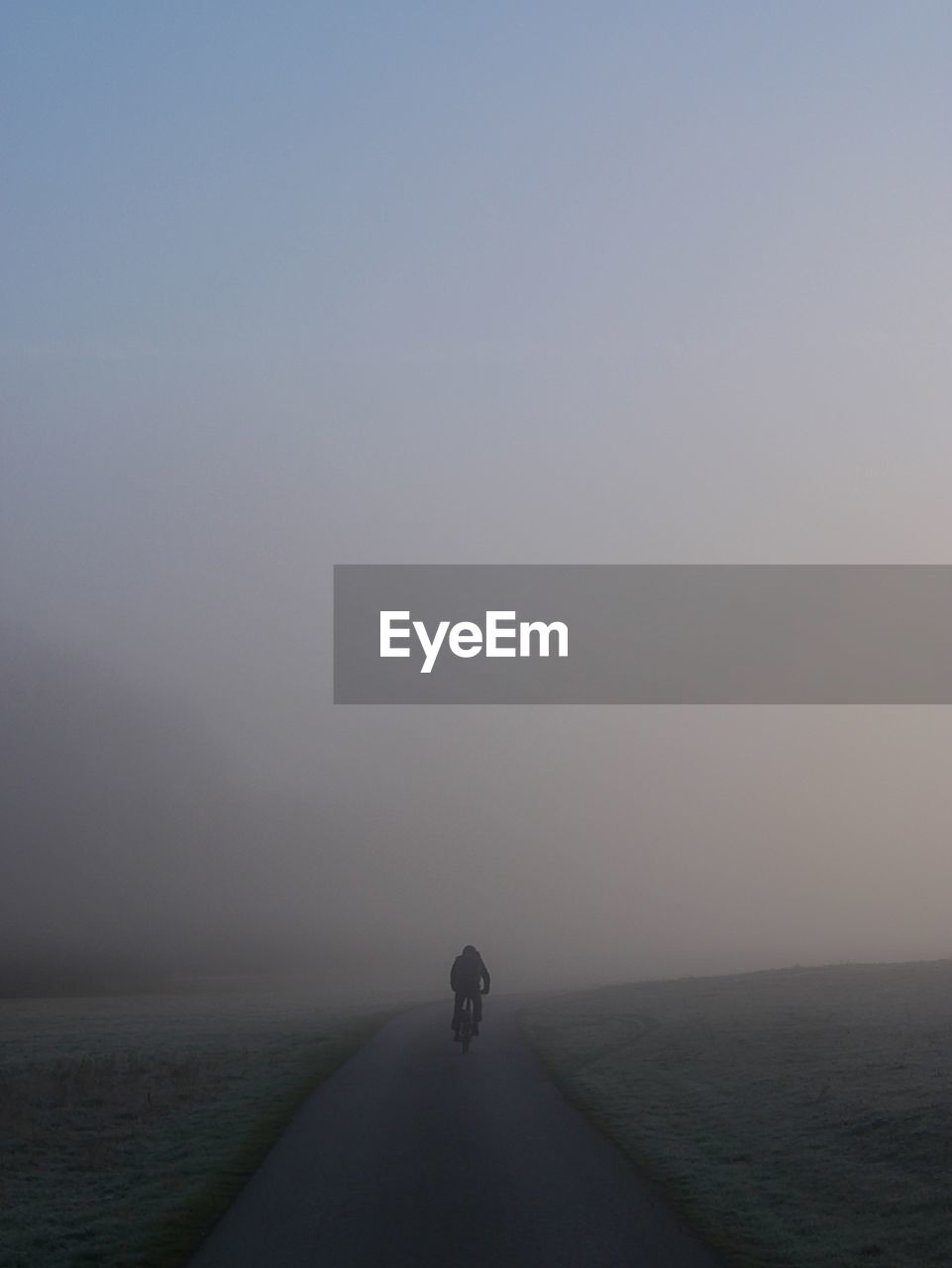 Rear view of man riding bicycle on road during foggy weather