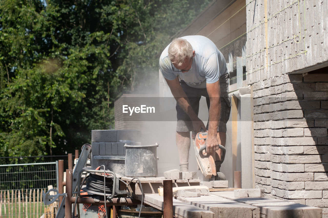 A grayhaired man saw bricks with a concrete saw of the right size for subsequent