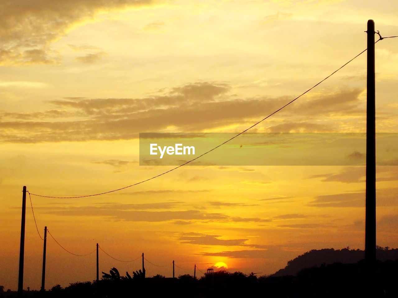 SILHOUETTE ELECTRICITY PYLON AGAINST ORANGE SKY