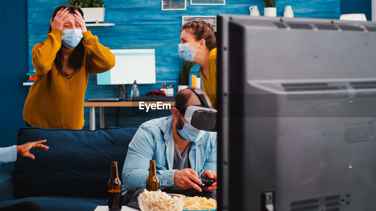 Man playing video game while wearing virtual reality simulator by women at home