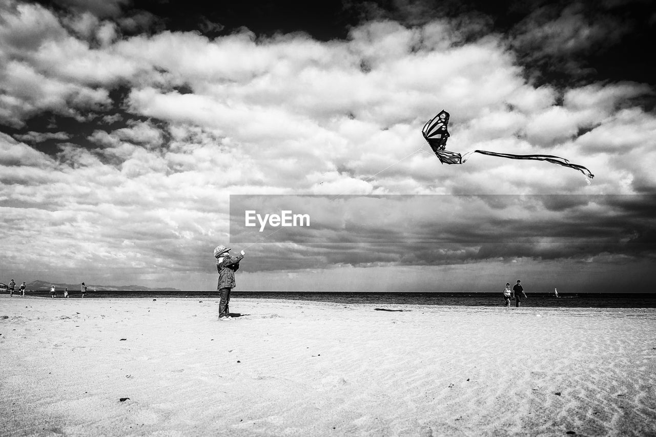Side view of boy flying kite while standing on beach