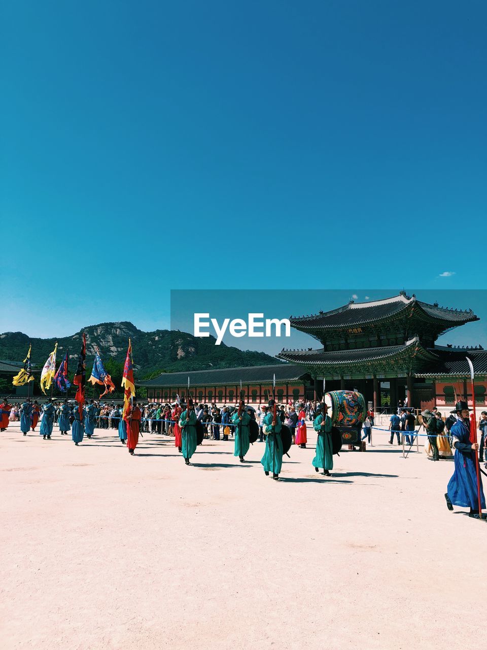 Group of people wearing traditional clothing in town against clear blue sky during sunny day