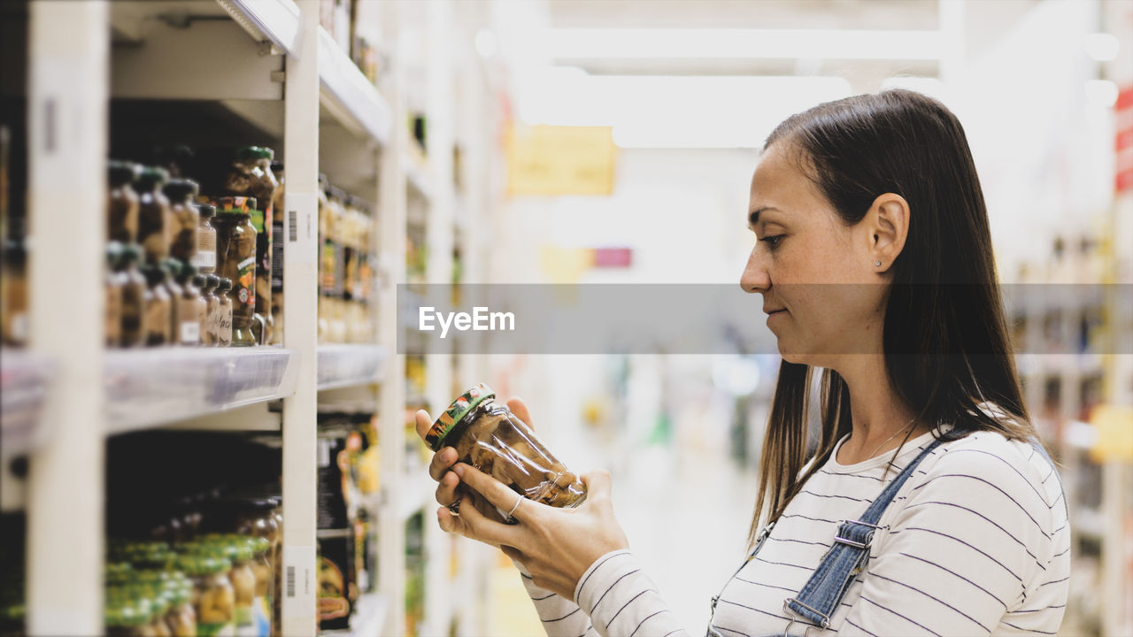 Side view of woman looking at bottle in supermarket