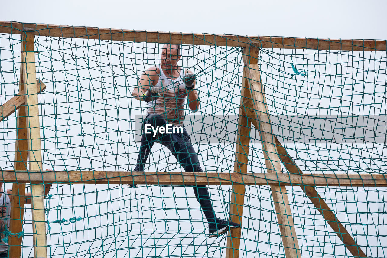 LOW ANGLE VIEW OF MAN CLIMBING ON METAL STRUCTURE