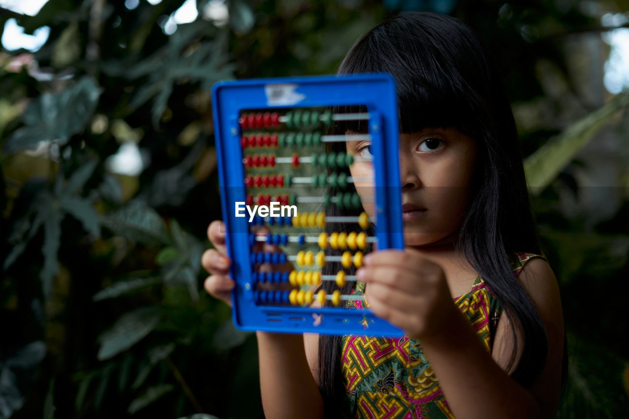 Close-up of girl playing with abacus against plants