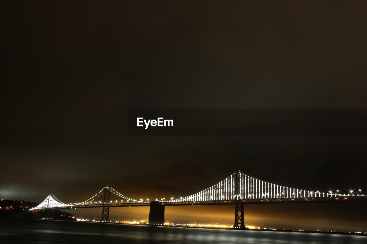 Illuminated oakland bay bridge over san francisco bay against sky at night