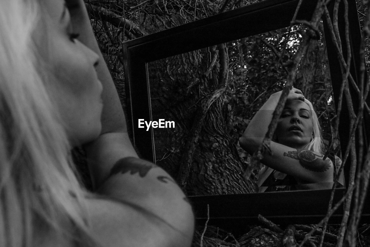 Young beautiful woman looking in mirror against tree branches in forest