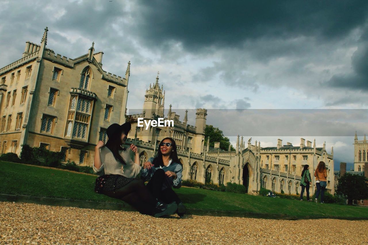 TOURISTS IN FRONT OF BUILDINGS AGAINST CLOUDY SKY