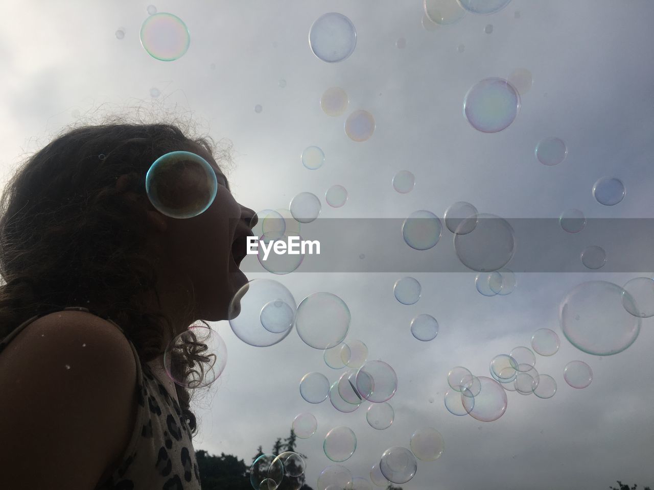 Low angle view of girl with mouth open by bubbles against sky