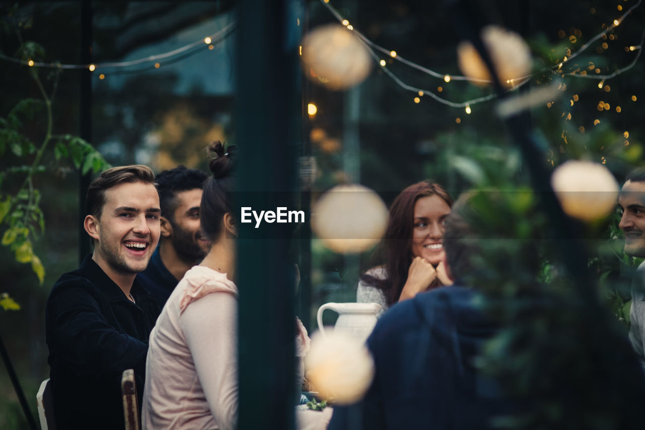 Happy multi-ethnic young friends sitting at dining table during party in back yard