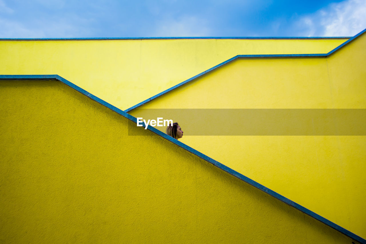 Low angle view of woman against yellow wall and sky