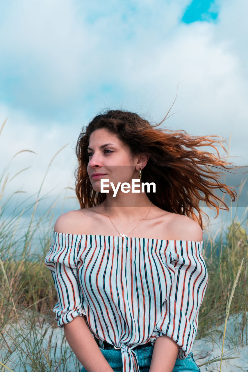 BEAUTIFUL YOUNG WOMAN STANDING AGAINST SKY DURING SUNRISE