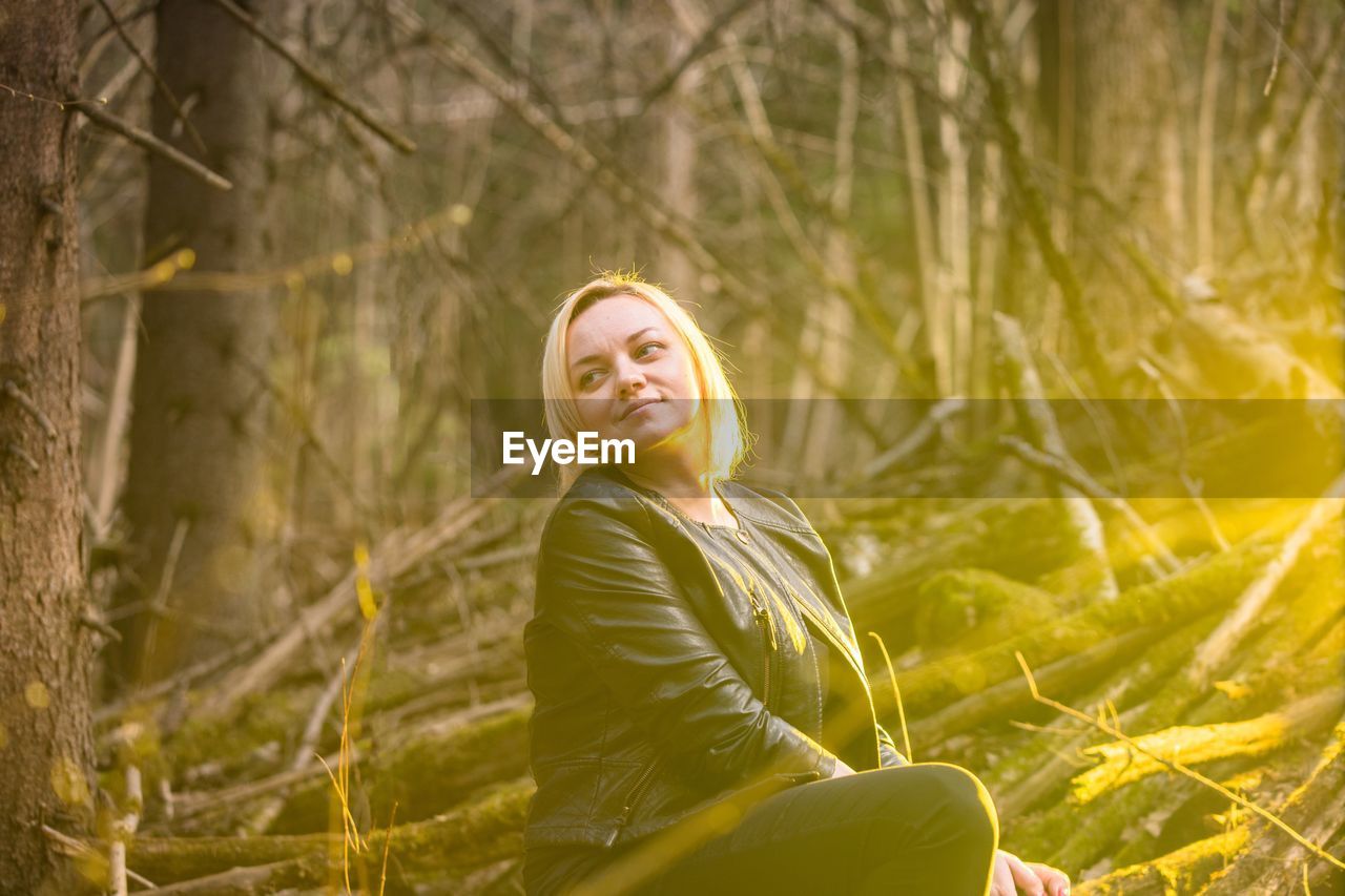 Smiling young woman looking away while sitting in forest