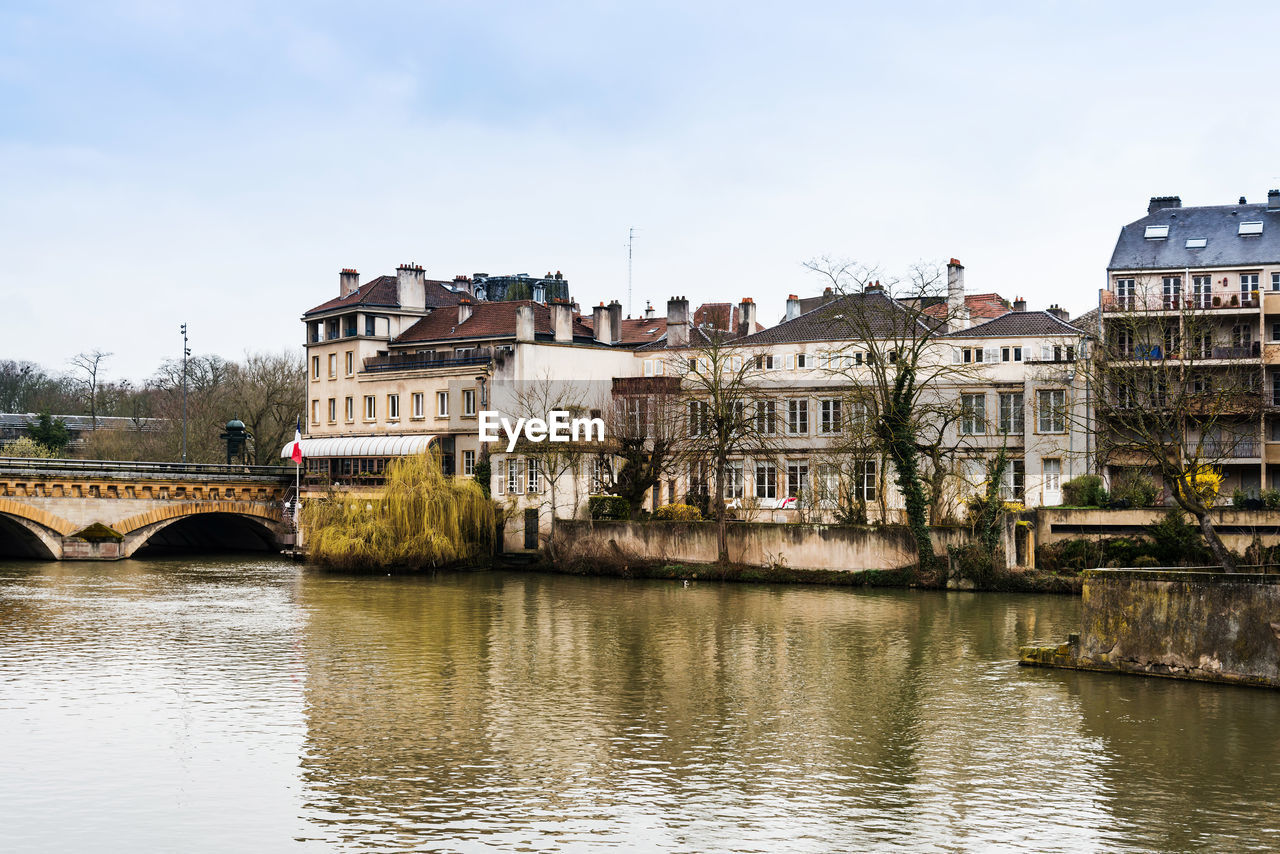 Bridge over river by buildings against sky