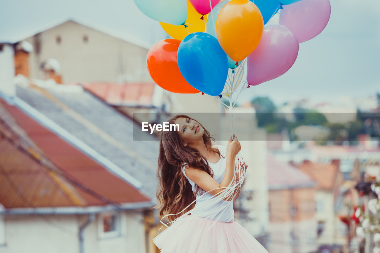 Portrait of smiling teenage girl holding balloons outdoors