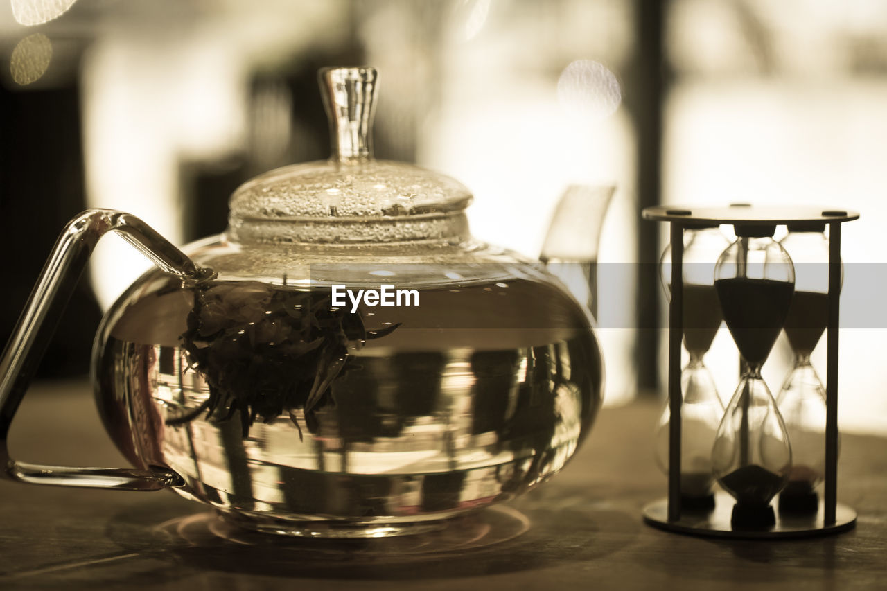 Close-up of herbal tea in pot by hourglass on table