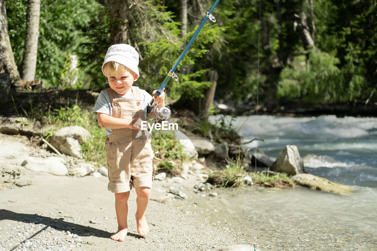 Little child boy fishing with a fishing rod on the mountain river on summer day