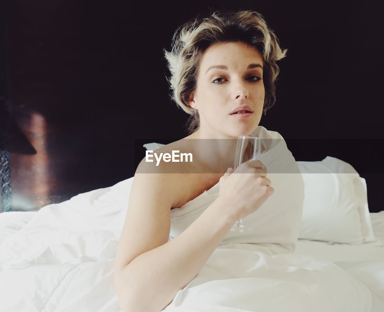 Portrait of a young woman sitting on bed drinking champagne 