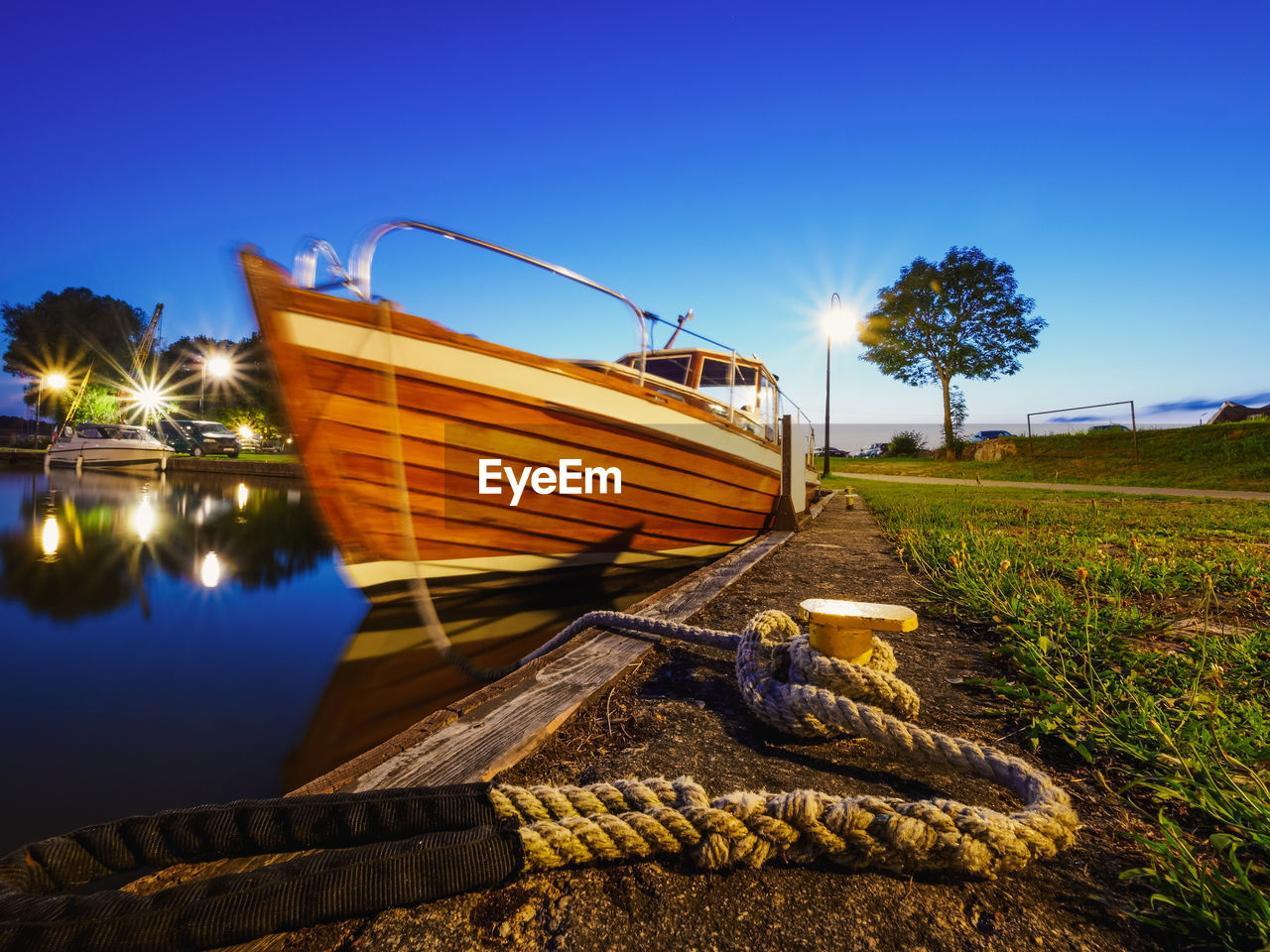 Wide view on metal bollard or hook on a quay where moored wooden motorboat, calm dusk view