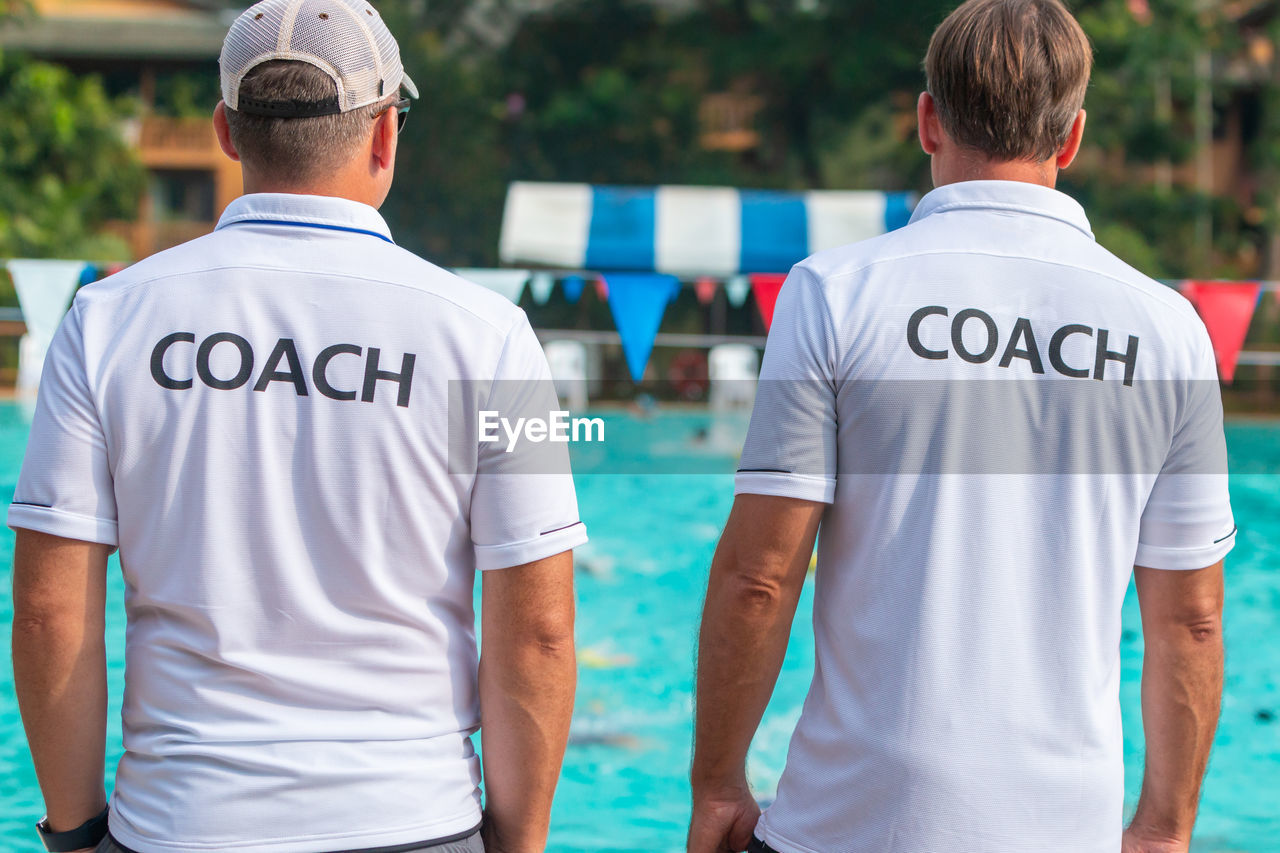 Rear view of men wearing t-shirts with coach text standing by swimming pool