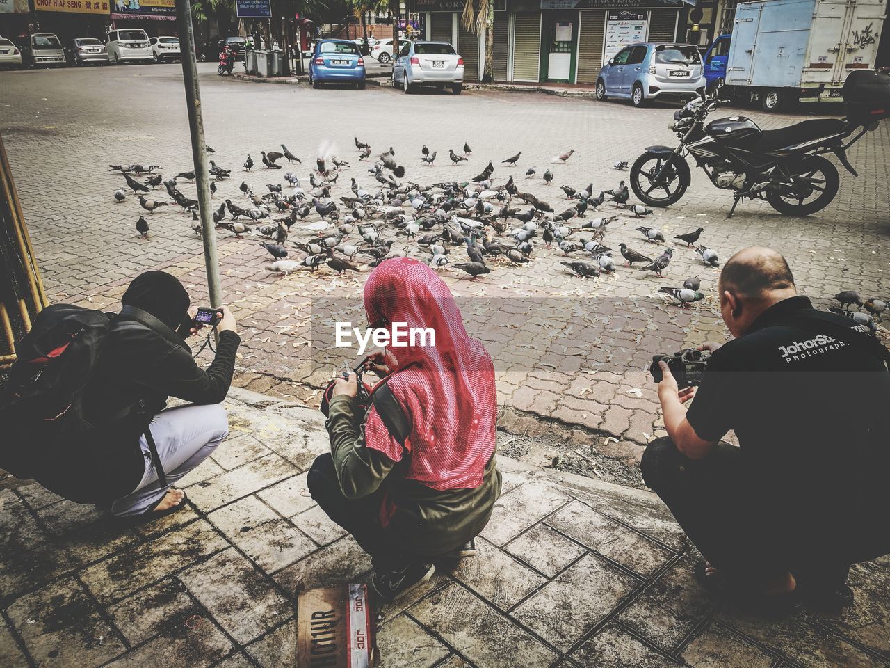 PEOPLE SITTING ON SIDEWALK BY STREET