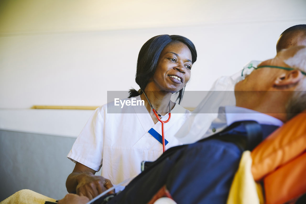 Smiling female doctor looking at mature patient on stretcher in hospital