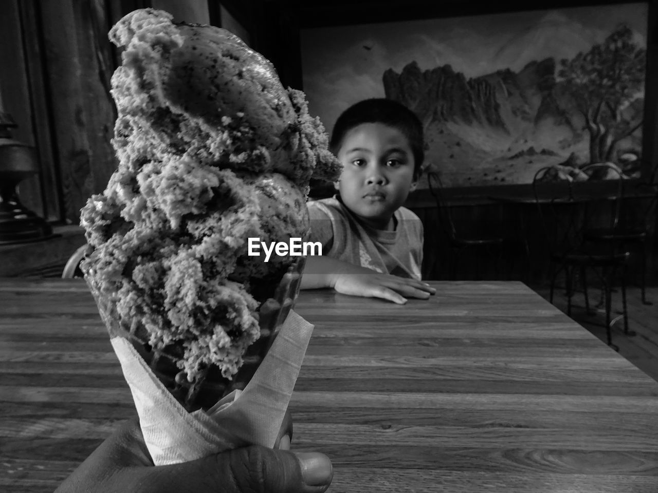 Cropped hand holding ice cream in front of boy at restaurant