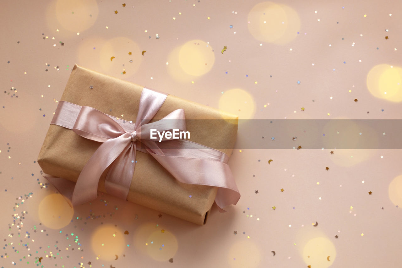 Valentines day, birthday or new year eve present in kraft paper with pink ribbon on beige background