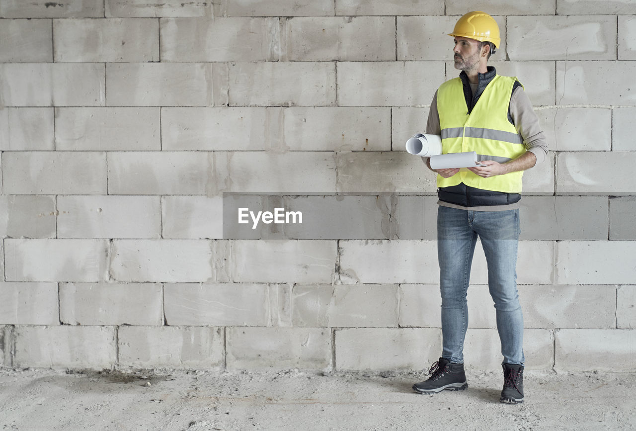 Male architect with blur print standing against wall