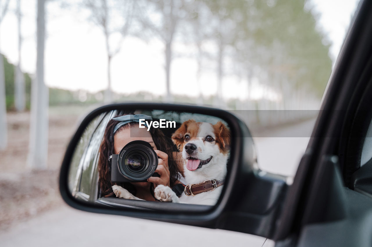 Woman photographing with dog reflecting in car