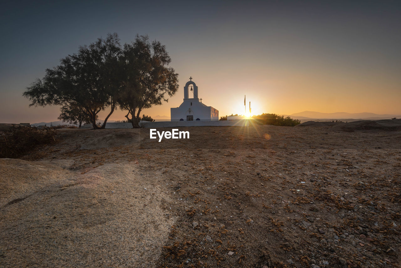 Greek church amidst trees and buildings against sky at sunset