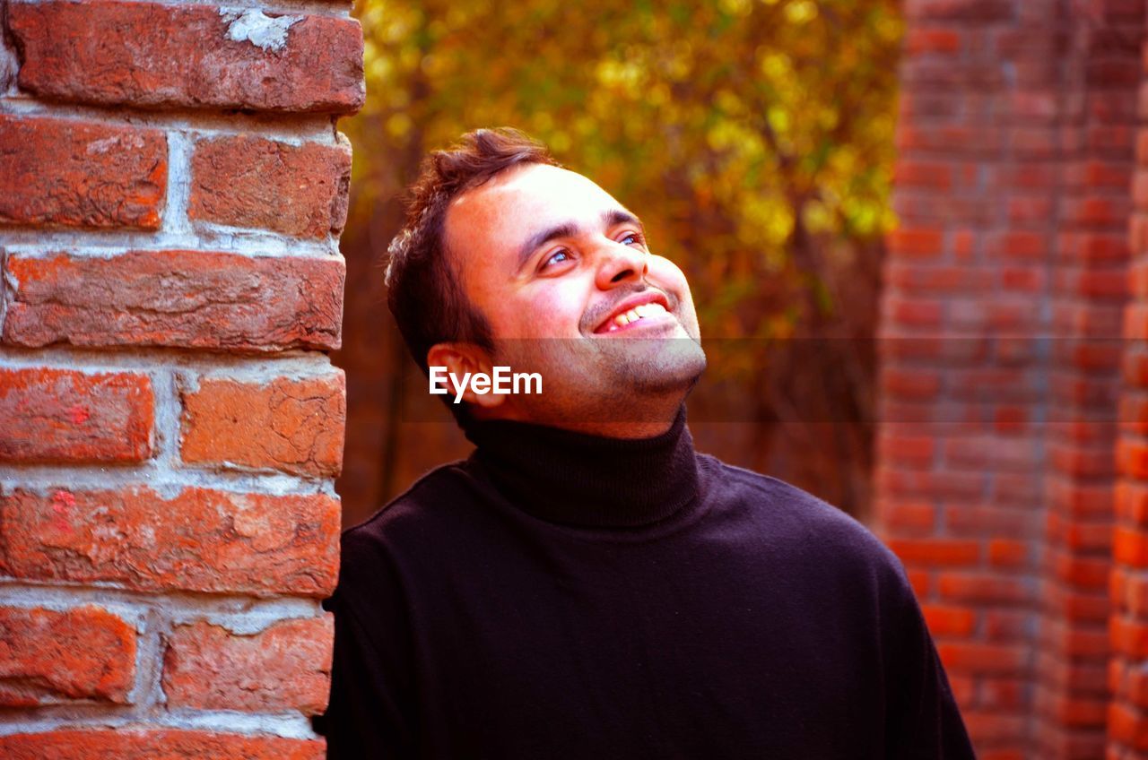 Close-up of smiling young man looking away by wall