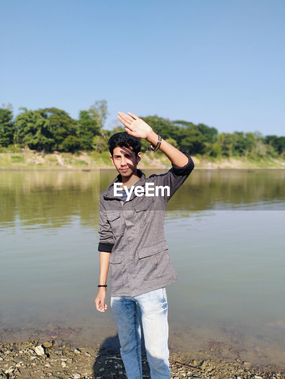 water, one person, lake, nature, casual clothing, adult, standing, leisure activity, day, full length, sky, young adult, smiling, copy space, hat, front view, lifestyles, outdoors, emotion, clothing, men, portrait, happiness, clear sky, reflection, plant, tree, looking, looking at camera, environment, beauty in nature, tranquility, beach, holiday, activity, sunny, vacation, sunlight, trip, holding, lakeshore, women