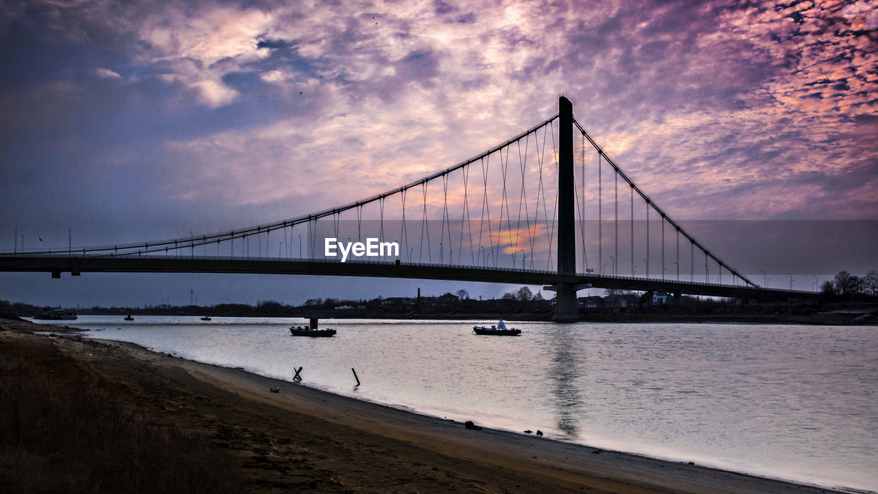 Suspension bridge over river against sky during sunset