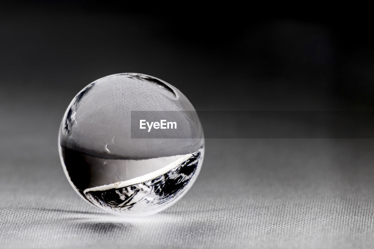 CLOSE-UP OF CRYSTAL BALL ON TABLE AGAINST GRAY BACKGROUND