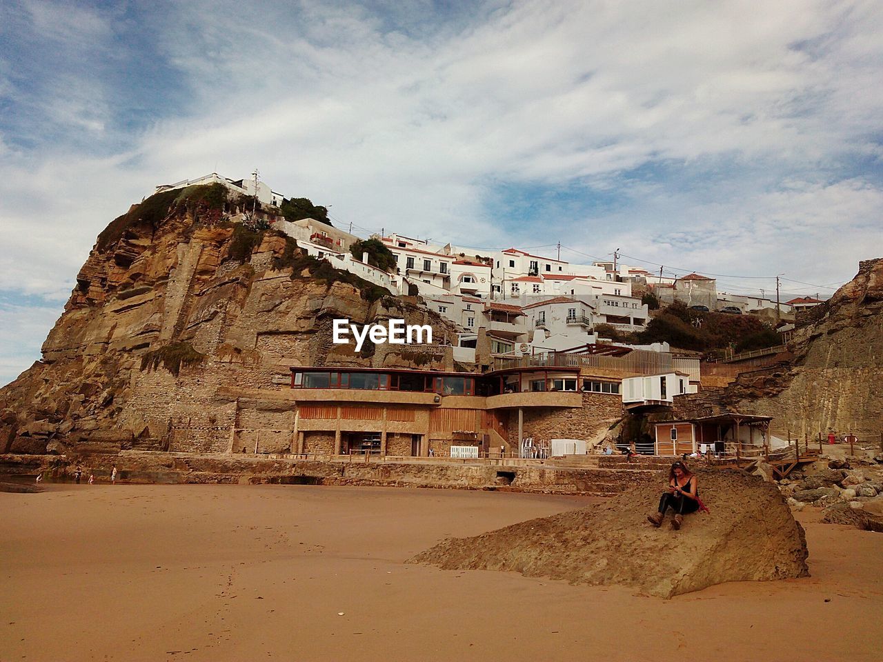 Woman sitting on rock against buildings at azenhas do mar
