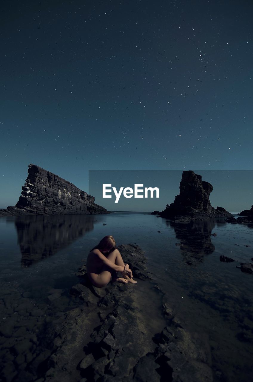 Side view of naked woman hugging self at rocky shore