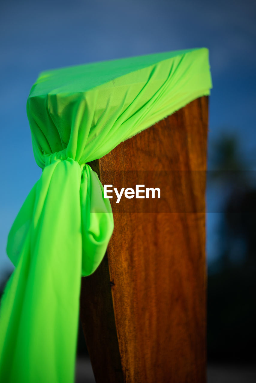 Close-up of green textile tied on wooden post against blue sky