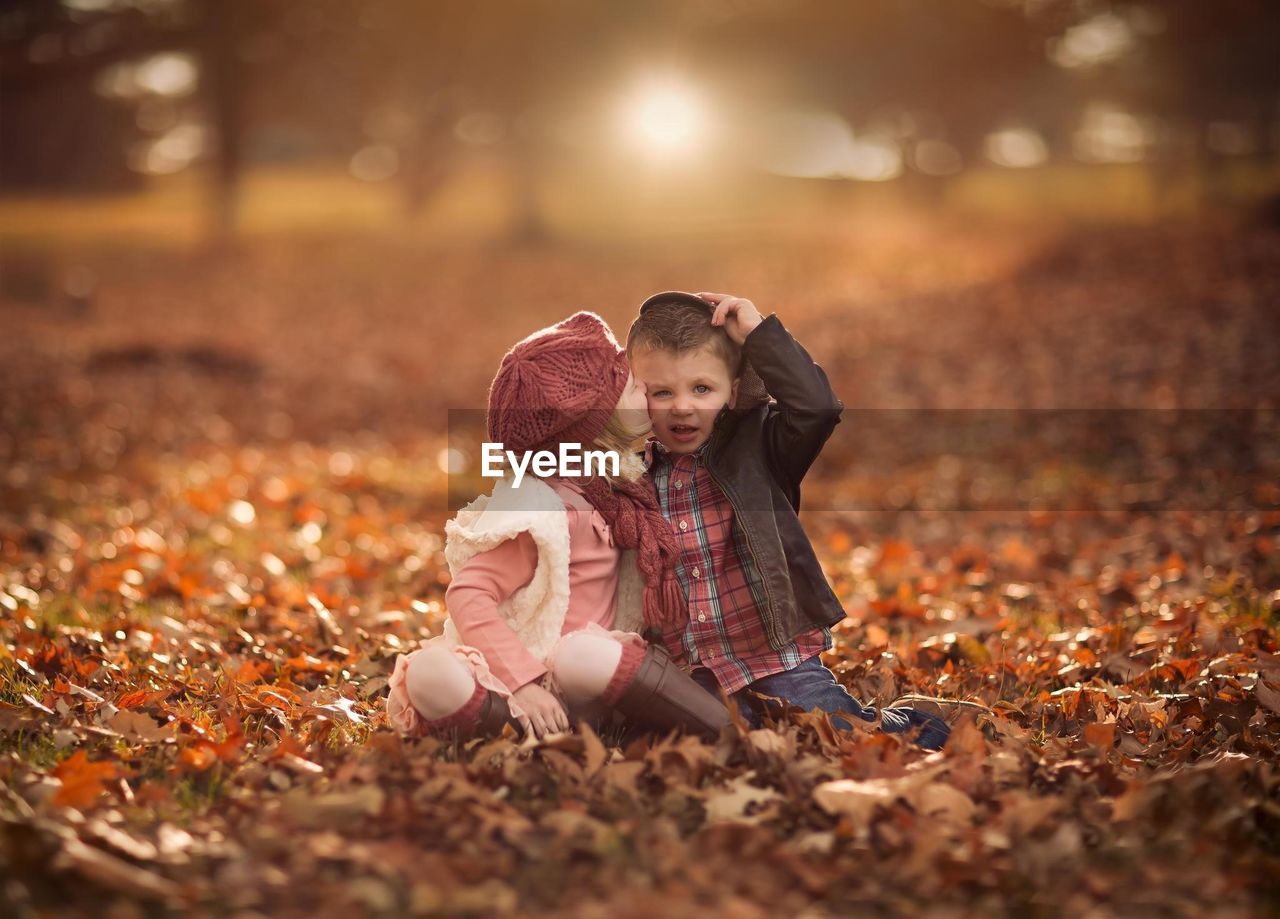 Girl kissing boy sitting on field during autumn